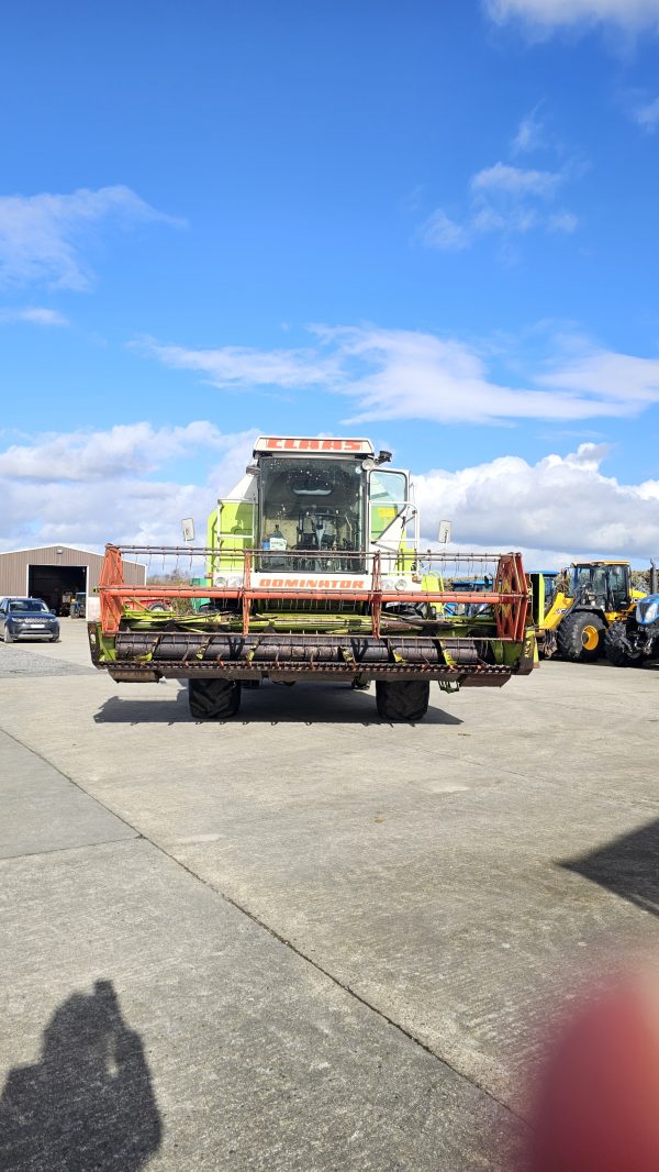 The front view of the Claas Dominator 98S combine harvester, highlighting its wide header, grain tank, and front wheels.