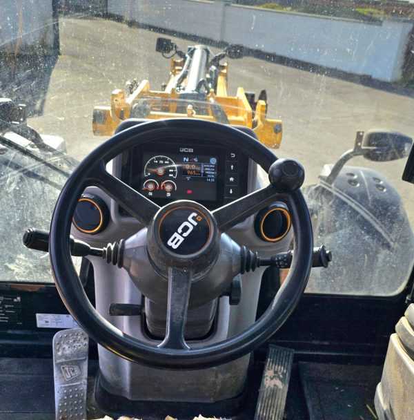 Inside view of a JCB tractor cabin, showcasing the steering wheel, display controls, and pedals for efficient operation.