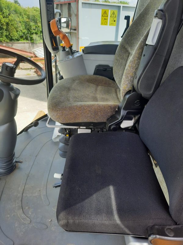 Interior view of the New Holland CS640 harvester cabin, showing one dark seat and a main grayish seat.