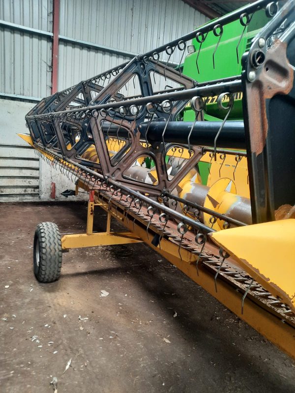 Side front view of a New Holland harvester, showcasing the large wheels and cutting machinery.